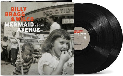 Vinyl album cover showing a child pushing another child on a hand cart in front of 3 other people and a large building (all in black & white) with orange text "Billy Bragg & Wilco" and white text "mermaid avenue vol. iii" with two black vinyl records sticking out the side of the sleeve.