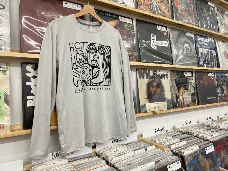 Light grey colored long sleeve shirt with "Hot Wax Summer" logo printed on the front in black ink, hung against a backdrop of a record wall