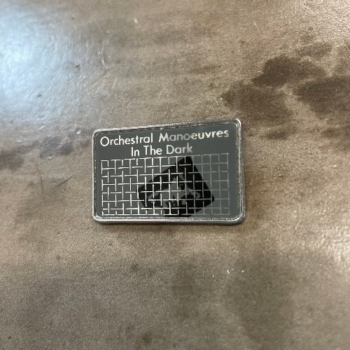 Orchestral Manoeuvres In The Dark Pin Silver Text against black backdrop