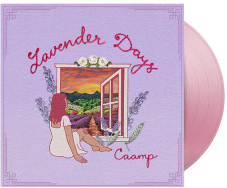 Vinyl record with cover featuring a person sitting by a window overlooking a lavender field and sunset, with 'Lavender Days' and 'Caamp' text. Shown with a pink vinyl record