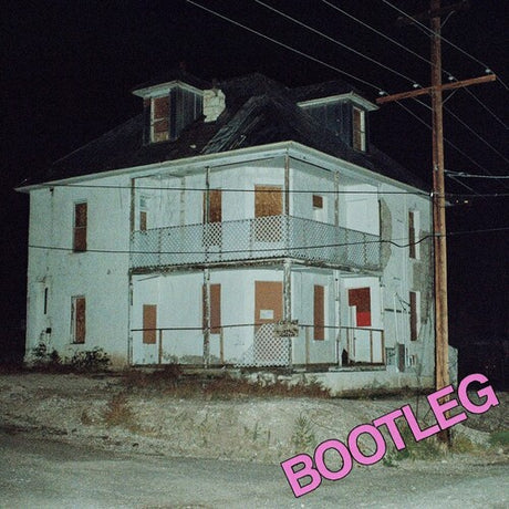 A nighttime photograph of a dilapidated white two-story house with boarded windows and a porch, set against a dark night sky with power lines and a utility pole. The word 'BOOTLEG' is written in large pink letters in the bottom right corner.