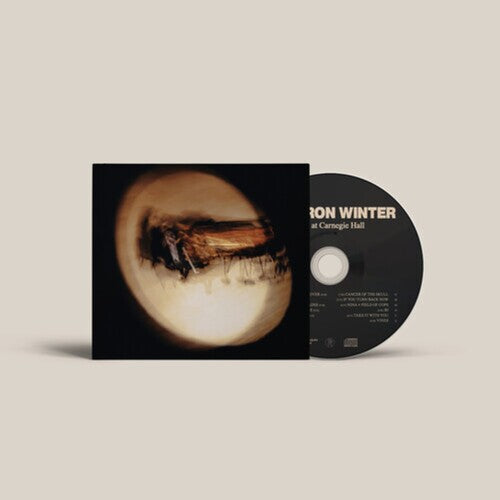 A CD album with its sleeve partially open, showing a black disc and cover art featuring a circular, abstract beige and brown image on a light warm gray background.