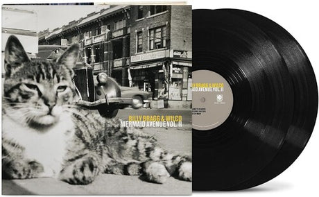 vinyl album cover showing a black and white image of a cat in front of a cityscape and car, with yellow text "Billy Bragg & Wilco' and white text "Mermaid Avenue Vol. II" and two black vinyl records sticking out of the side of the sleeve