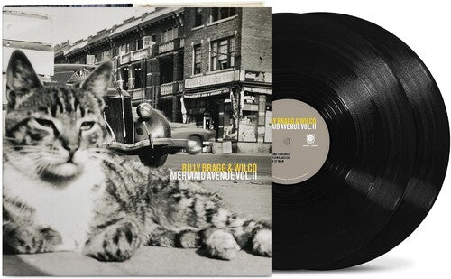 vinyl album cover showing a black and white image of a cat in front of a cityscape and car, with yellow text "Billy Bragg & Wilco' and white text "Mermaid Avenue Vol. II" and two black vinyl records sticking out of the side of the sleeve
