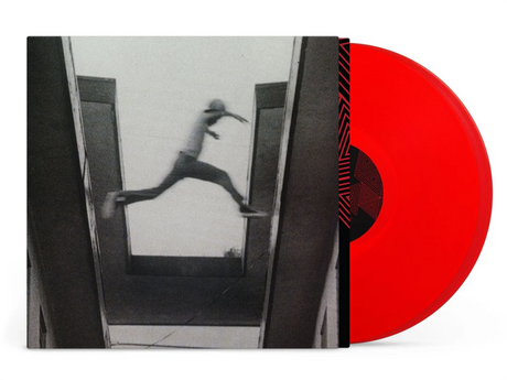 Red vinyl record with a black and white image of a person jumping from one building to another on the cover