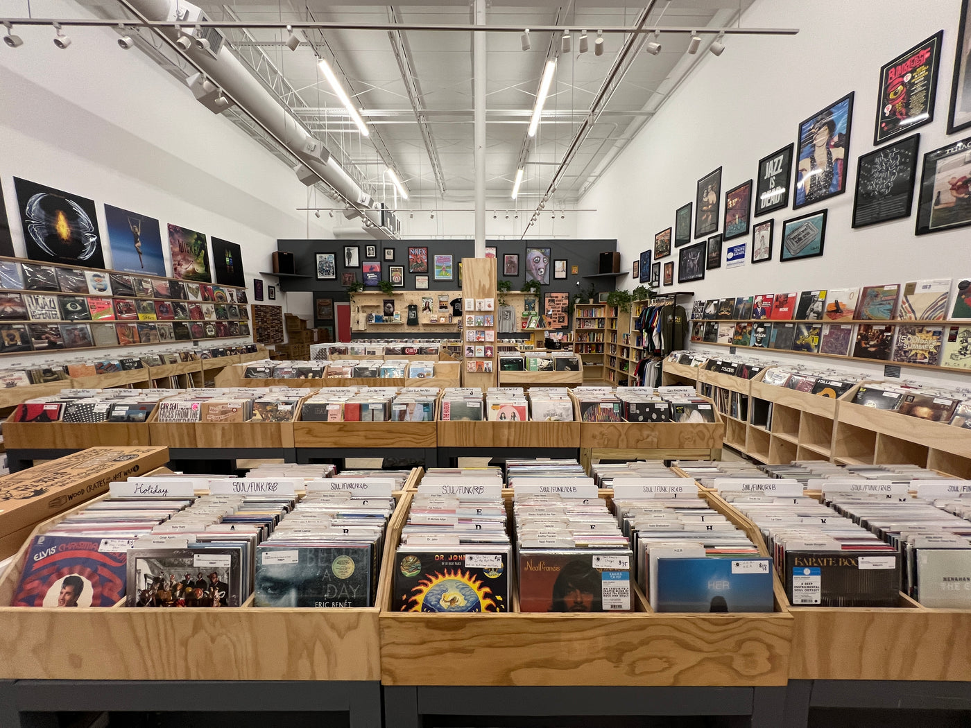 image depicting Rust & Wax Record Shop Retail floor, including wooden record bins filled with records, records on the walls, posters on the walls, and miscellaneous merchandise in the far back corners.