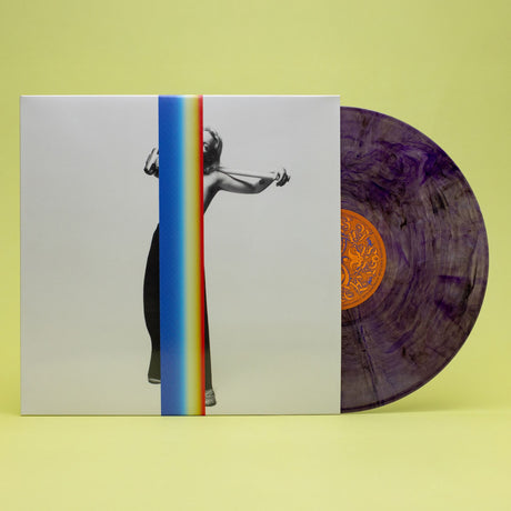 A vinyl record album shown with its outer sleeve and the record partially pulled out. The sleeve features a black-and-white photo of a woman with a vertical rainbow stripe running through the center, and the vinyl itself is purple with a gold center label.