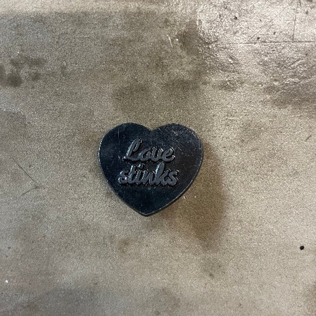 Love Stinks pin - Heart shape black backdrop with dark silver text
