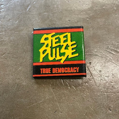 Steel Pulse Pin - Front Image Yellow and red text against green and black backdrop