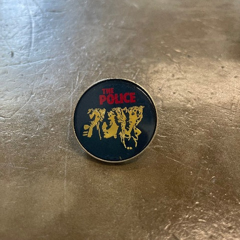 The Police Enamel Pin - Front Red text and gold band members against black backdrop